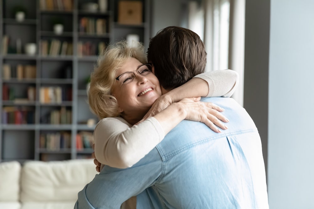 A senior woman hugs her adult son during a visit